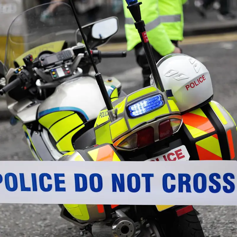 Police motorcycle parked behind 'POLICE DO NOT CROSS' tape at a crime scene.