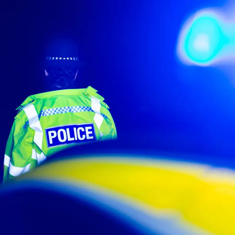Police officer in high-visibility jacket at night with flashing blue lights.