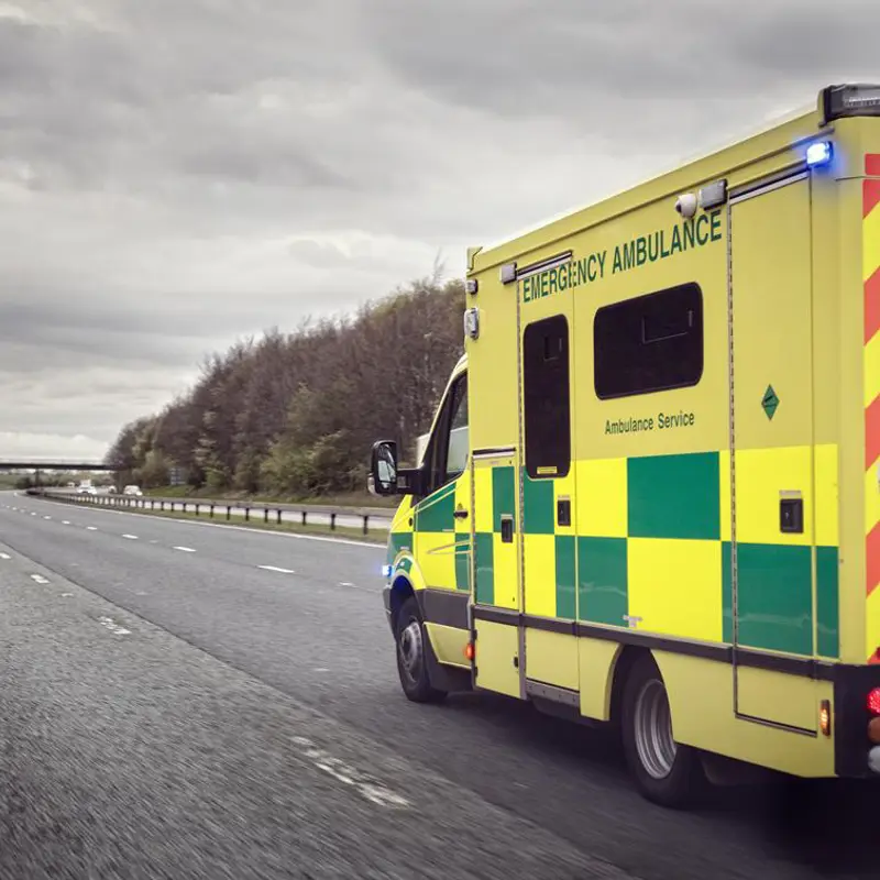 Emergency ambulance with flashing lights driving on a highway.