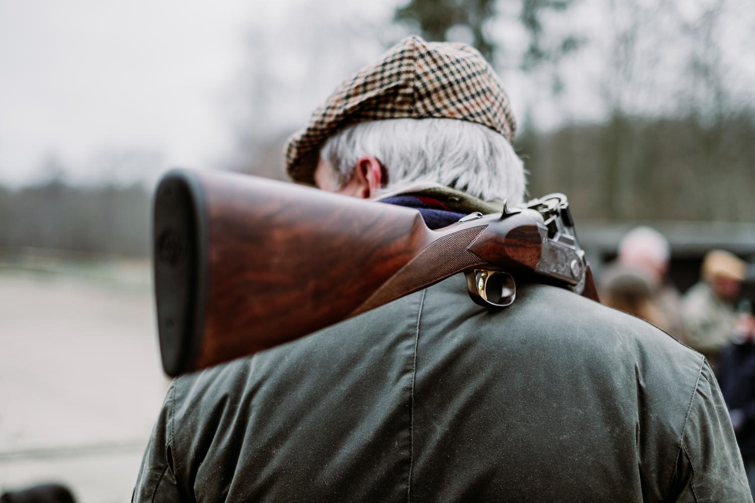 Man in country attire carrying a shotgun over his shoulder.