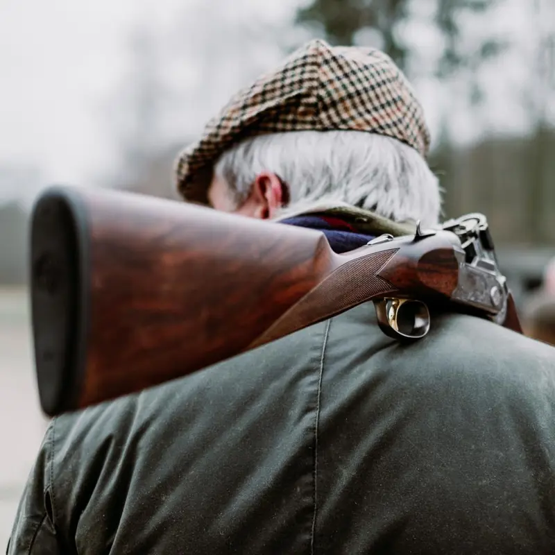 Man in country attire carrying a shotgun over his shoulder.