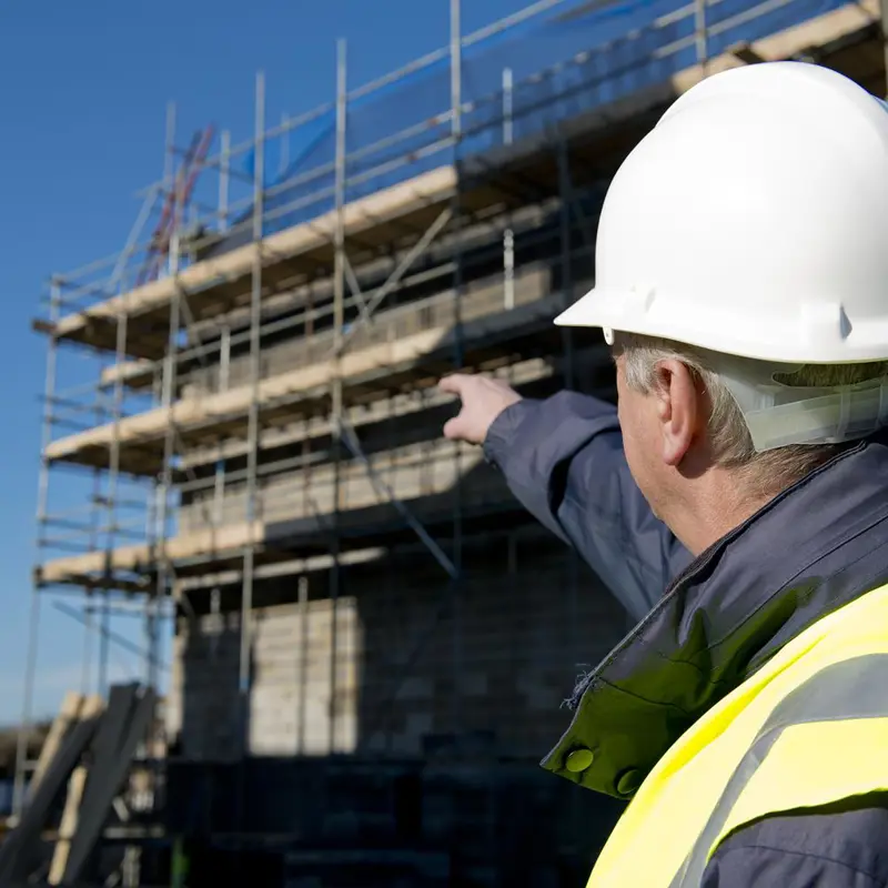 Construction worker in a hard hat and high-visibility vest pointing at a building under construction.