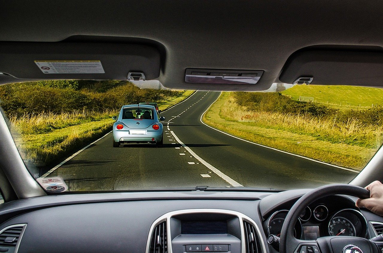 Driver's perspective of a winding rural road with a blue car ahead.