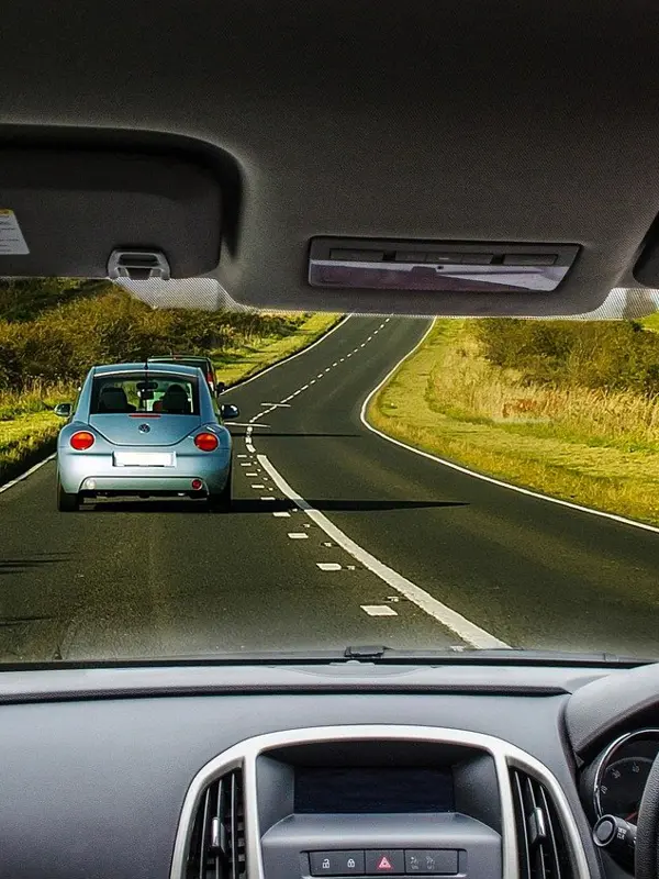 Driver's perspective of a winding rural road with a blue car ahead.