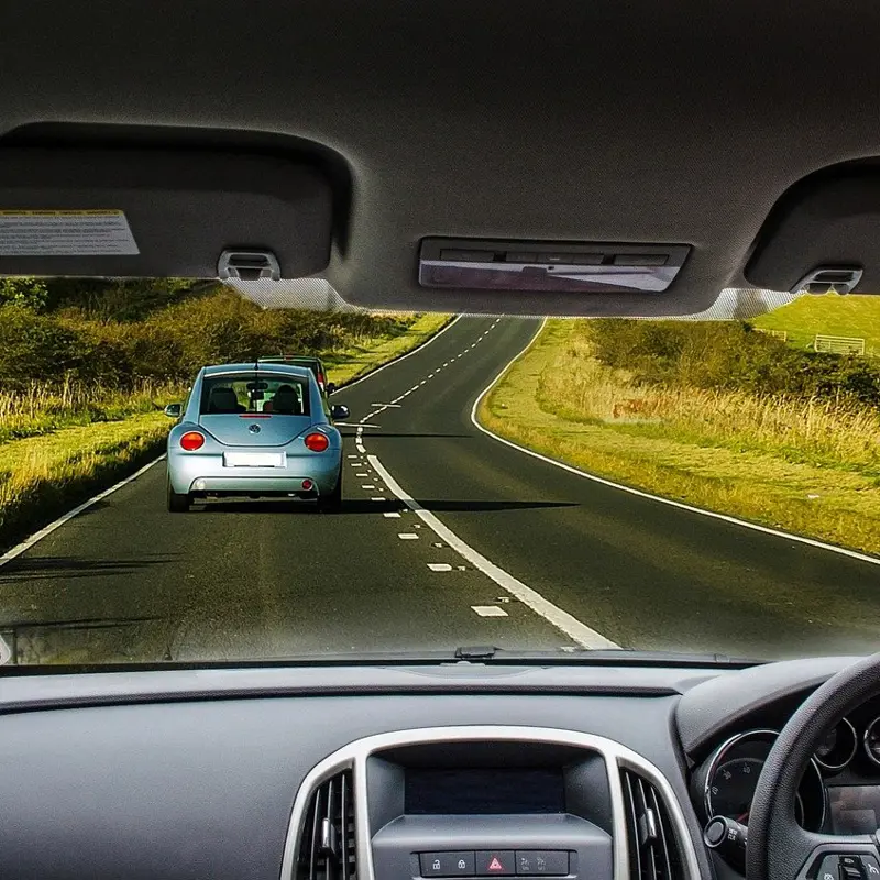 Driver's perspective of a winding rural road with a blue car ahead.