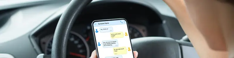 Driver holding the steering wheel while texting on a smartphone.