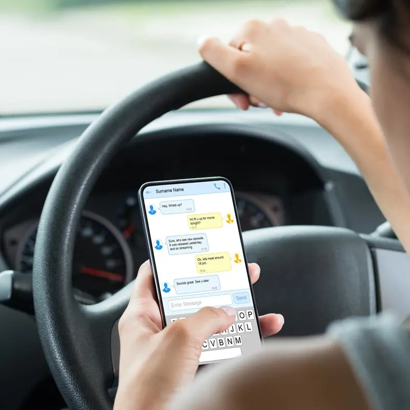 Driver holding the steering wheel while texting on a smartphone.