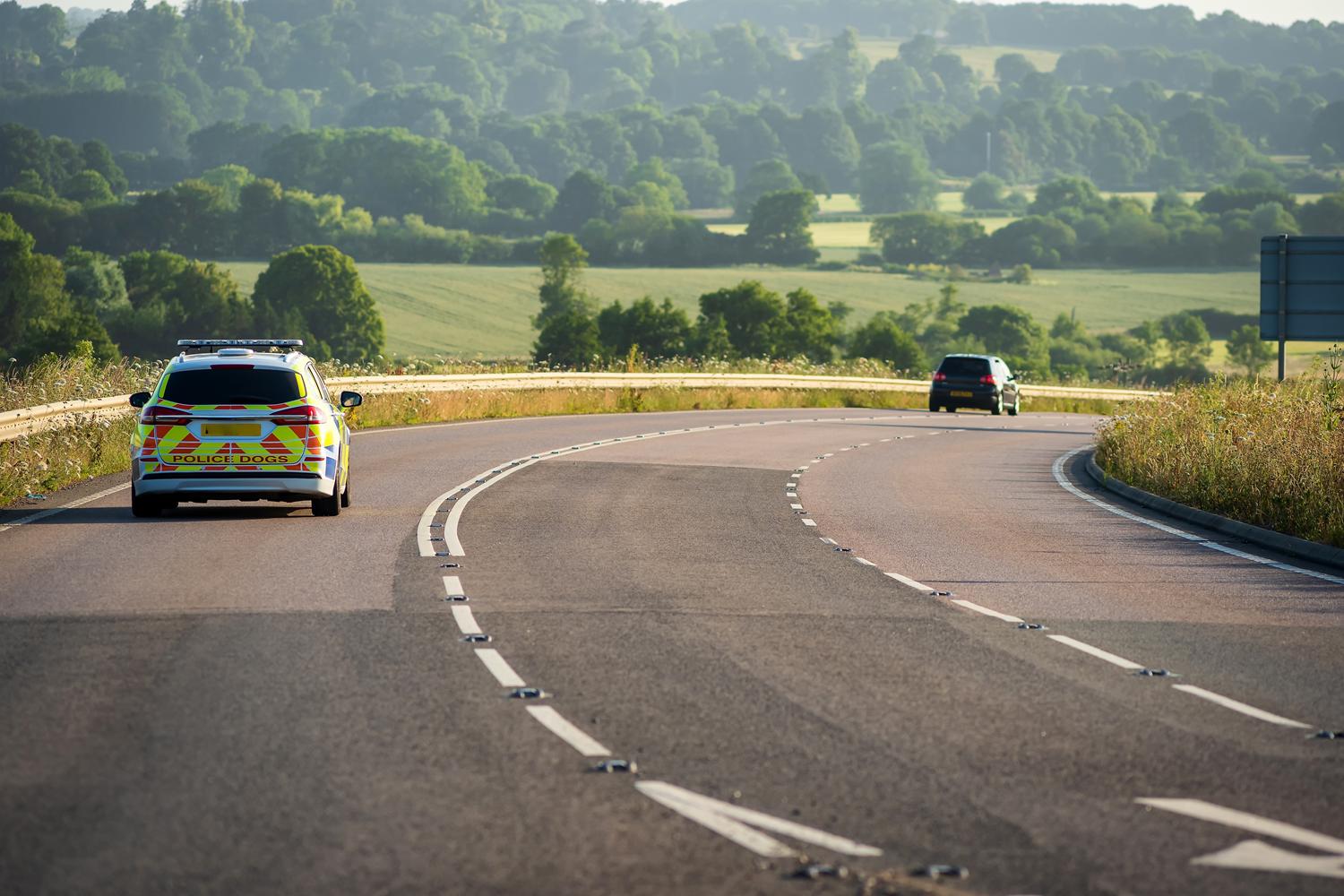 Police vehicle and another car driving on a winding rural road.