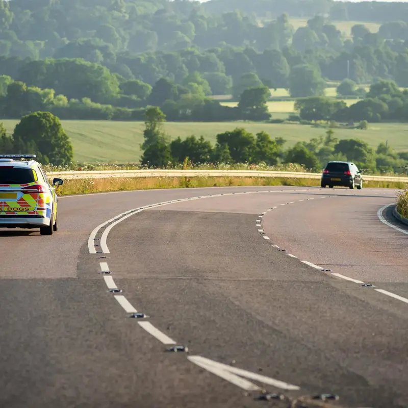 Police vehicle and another car driving on a winding rural road.