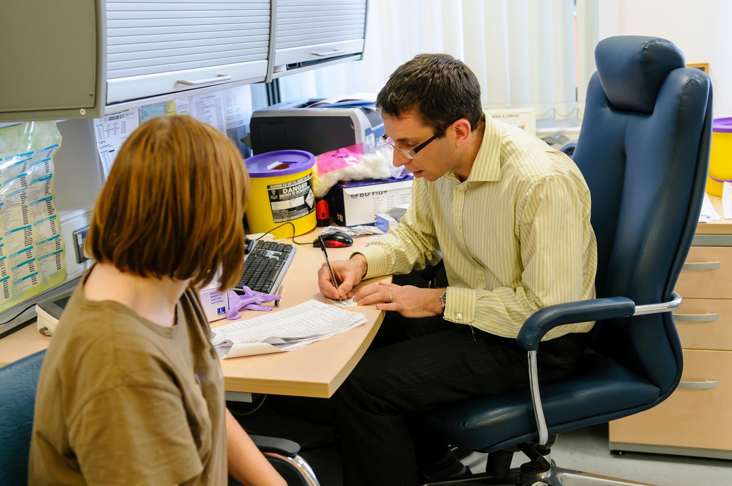 Doctor in an office writing a prescription while consulting with a patient.