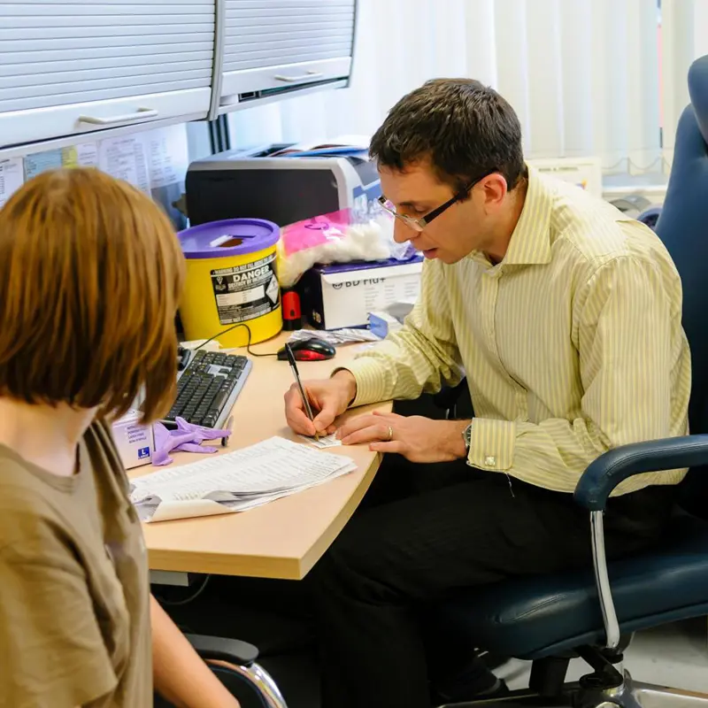 Doctor in an office writing a prescription while consulting with a patient.