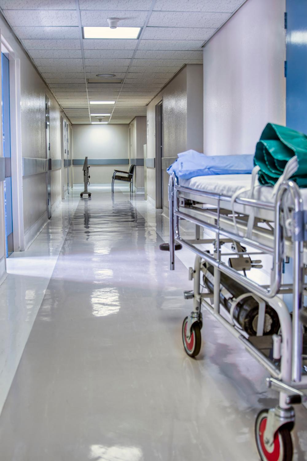 Hospital corridor with an empty stretcher and a chair in the distance.