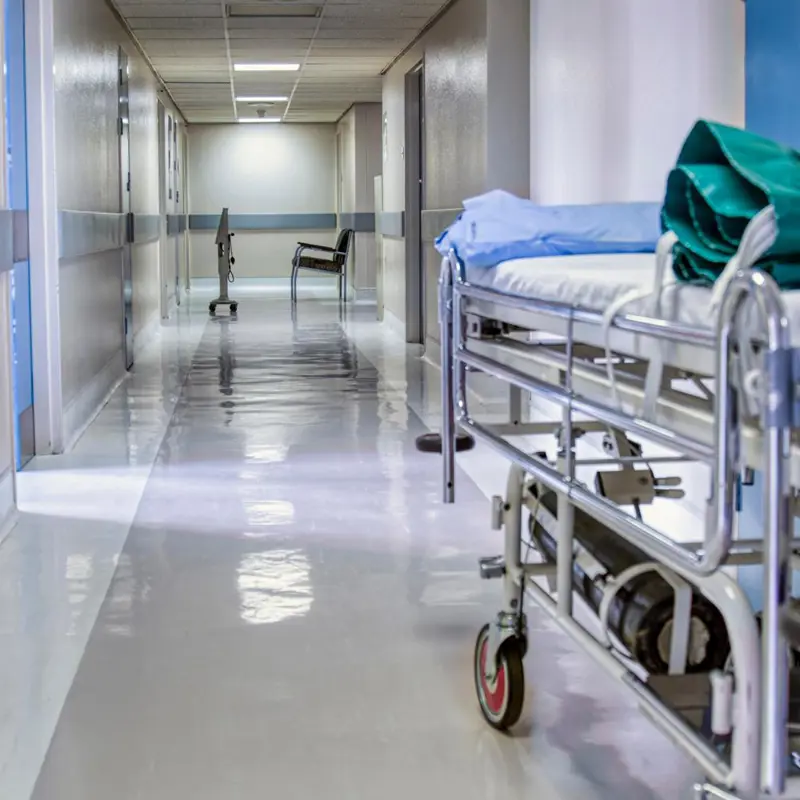 Hospital corridor with an empty stretcher and a chair in the distance.
