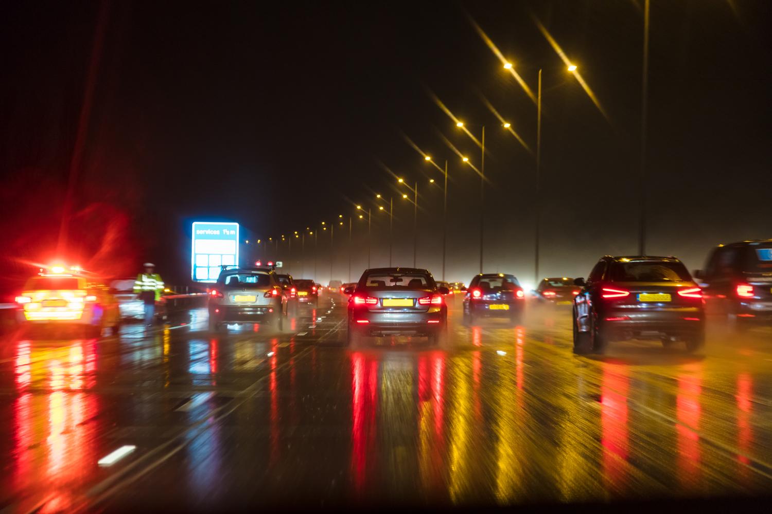 Busy highway at night with wet roads reflecting car and street lights.