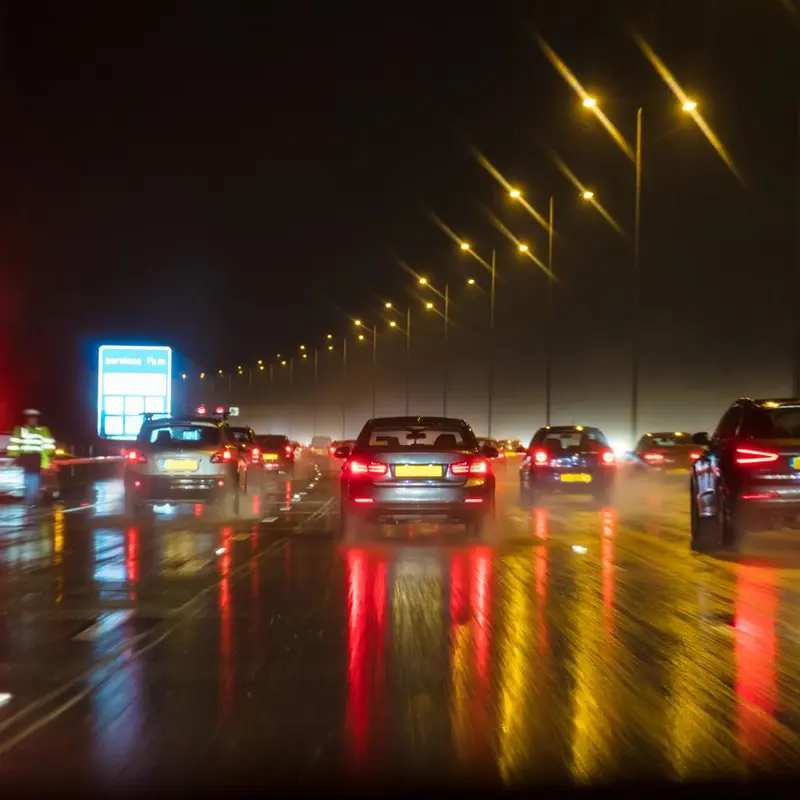Busy highway at night with wet roads reflecting car and street lights.