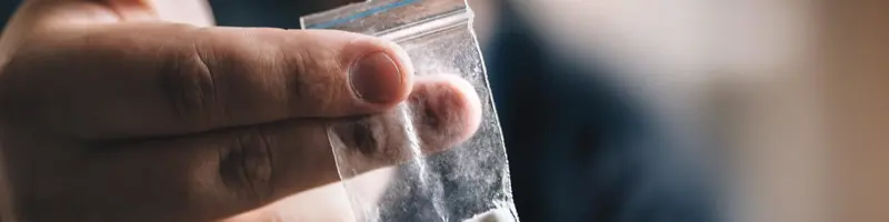 Close-up of a person holding a small plastic bag containing white powder.