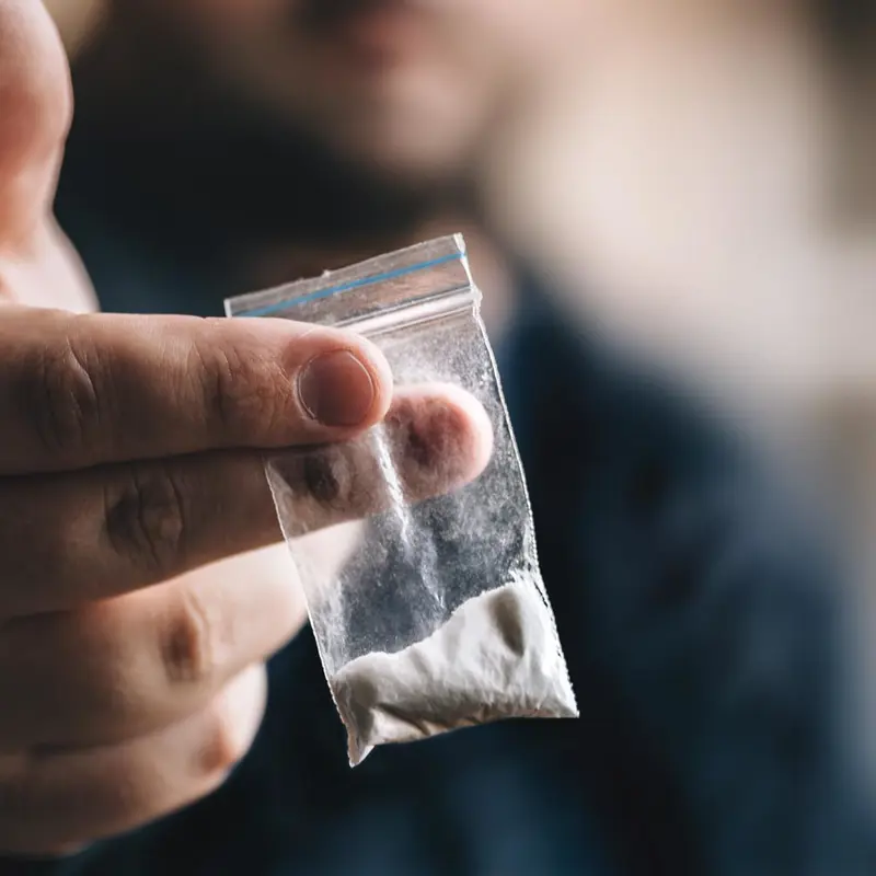 Close-up of a person holding a small plastic bag containing white powder.