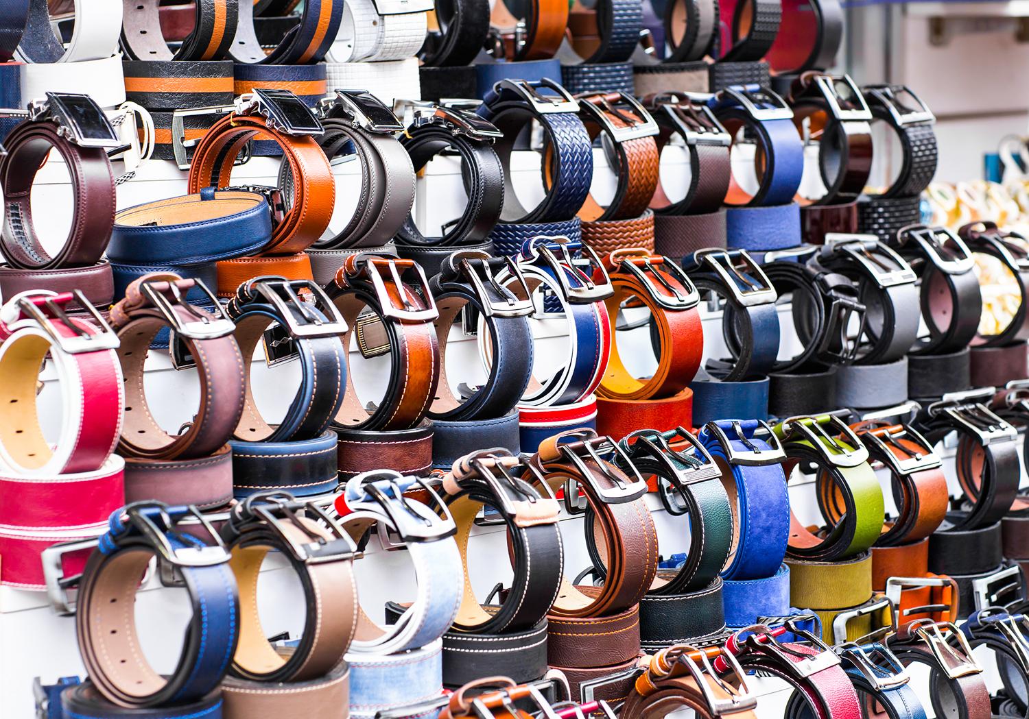 Display of various leather belts with metal buckles at a market stall.