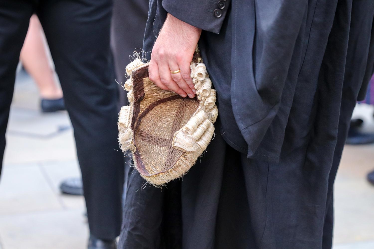 Barrister in black robes holding a traditional legal wig.