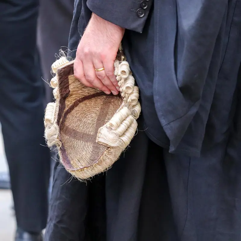 Barrister in black robes holding a traditional legal wig.