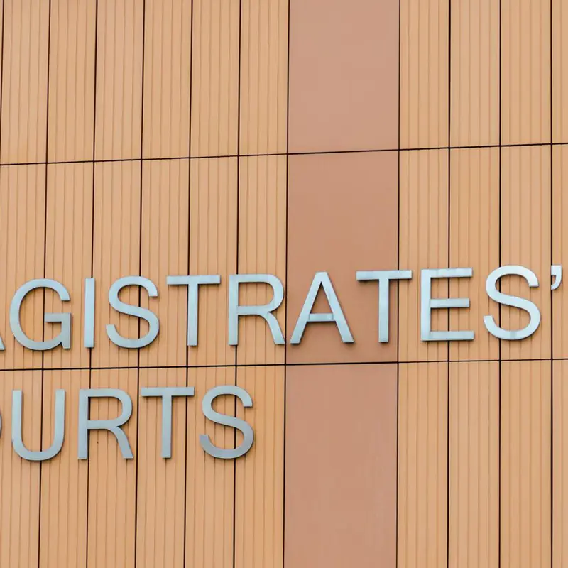 Sign reading 'MAGISTRATES' COURTS' on a modern building facade.