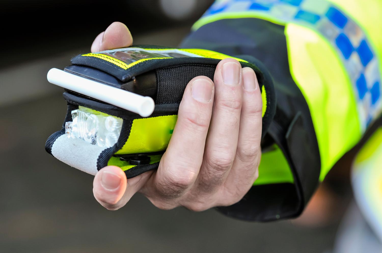 Police officer holding a breathalyser device for roadside alcohol testing.