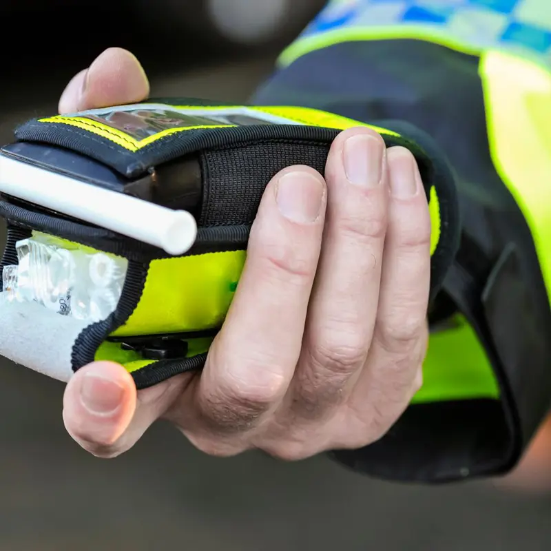 Police officer holding a breathalyser device for roadside alcohol testing.