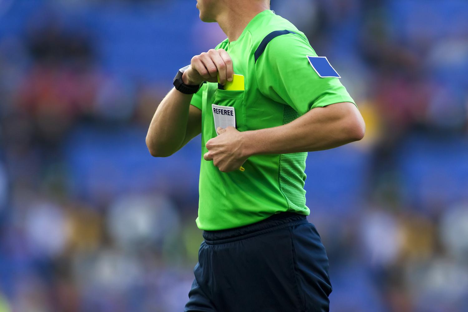 Football referee in a green uniform pulling out a yellow card during a match.