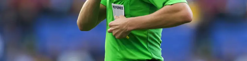 Football referee in a green uniform pulling out a yellow card during a match.