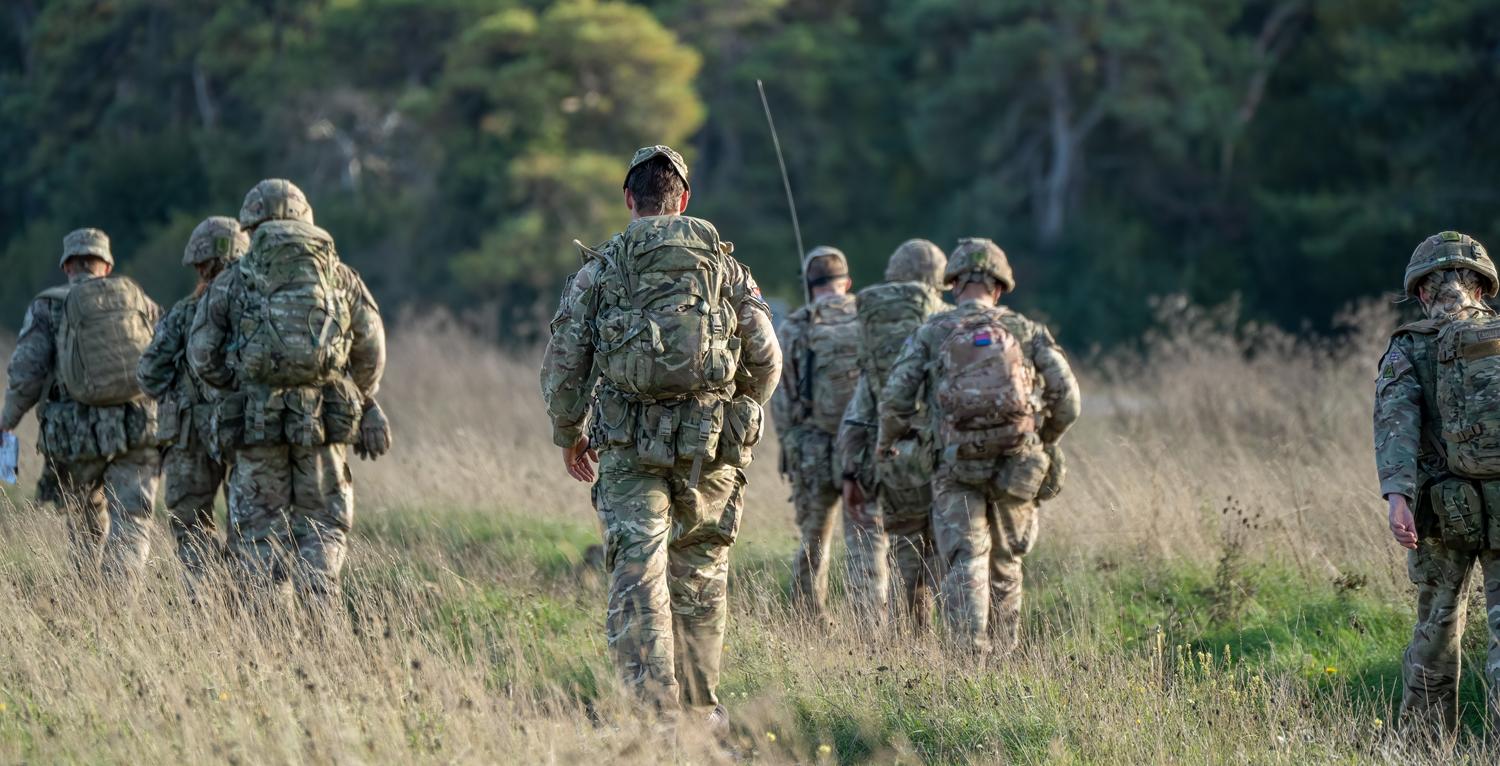 Group of soldiers in camouflage gear patrolling through a grassy field.