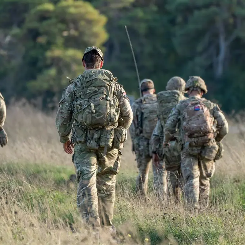 Group of soldiers in camouflage gear patrolling through a grassy field.