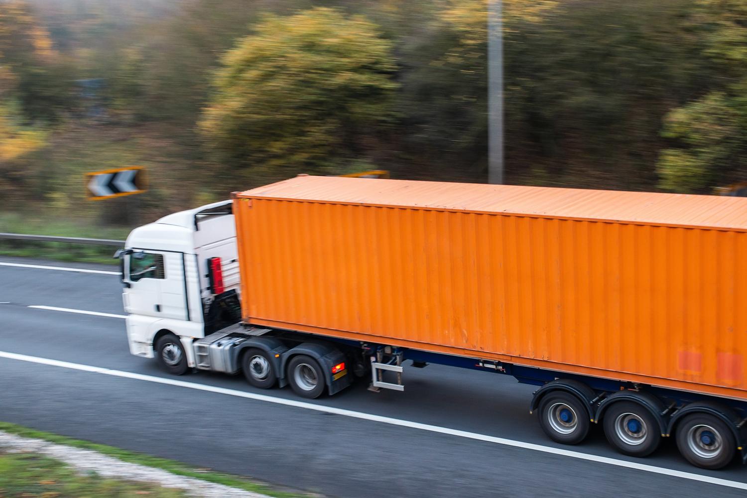 White semi-truck with an orange shipping container driving on a highway.