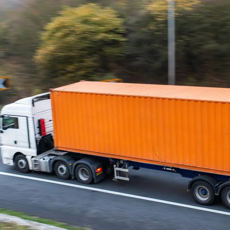 White semi-truck with an orange shipping container driving on a highway.