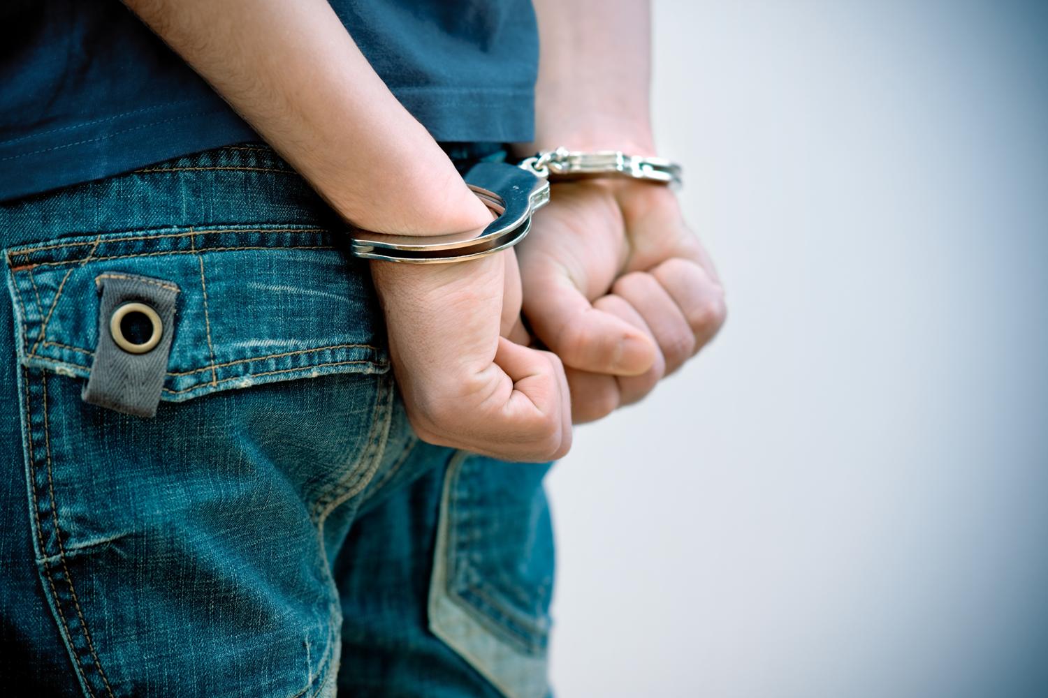 Close-up of a person's hands cuffed behind their back with metal handcuffs.