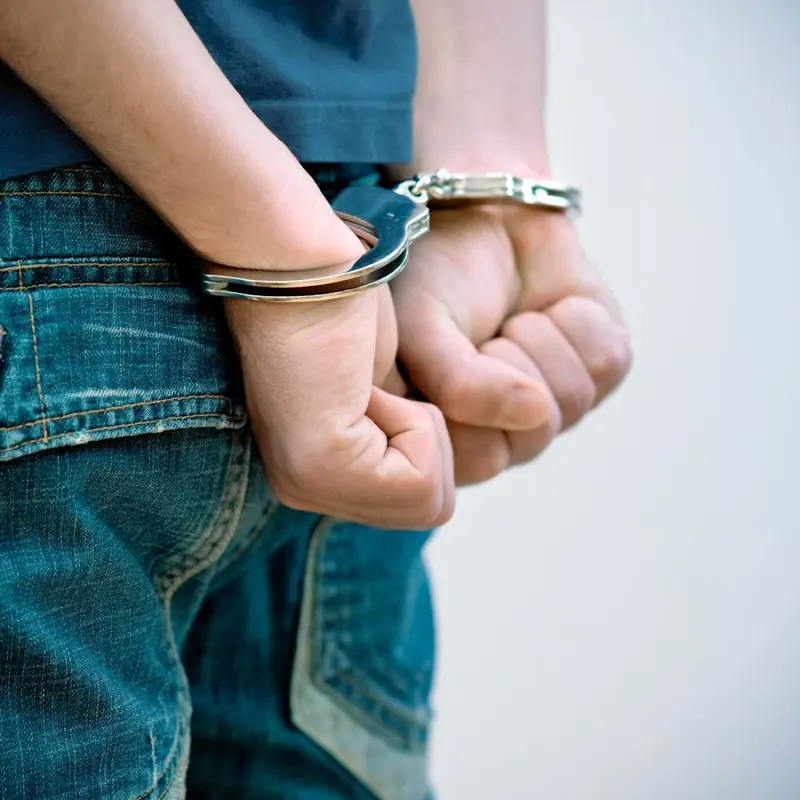 Close-up of a person's hands cuffed behind their back with metal handcuffs.