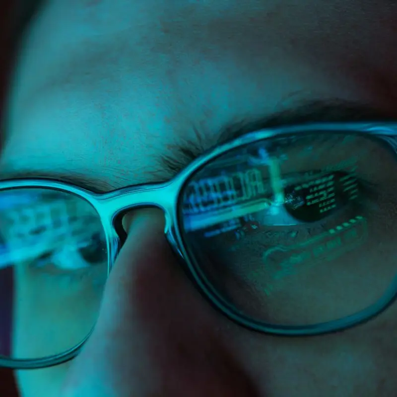 Close-up of a person wearing glasses with computer code reflecting in the lenses.