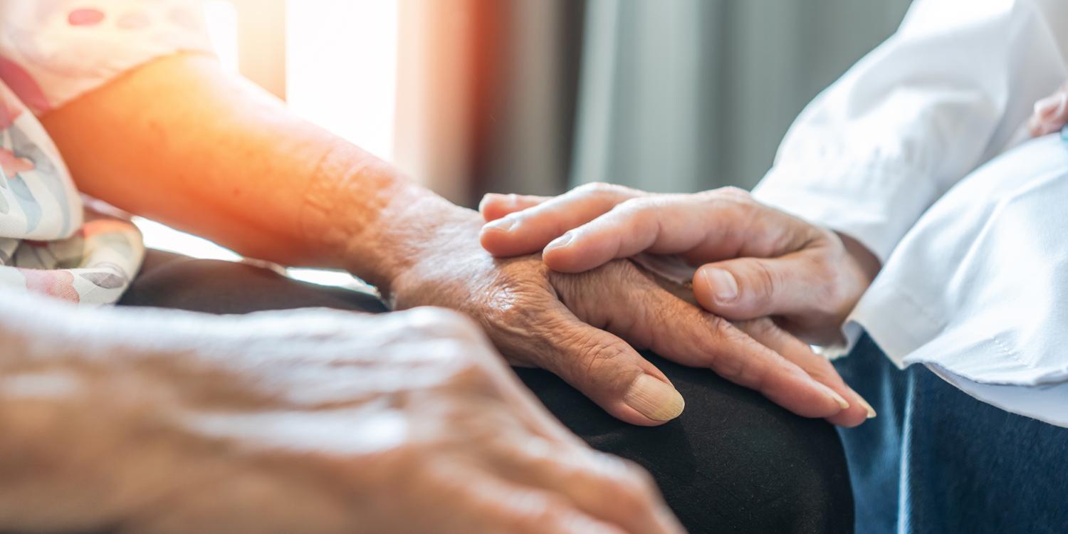 Close-up of an elderly person’s hand being comforted by a caregiver’s touch.
