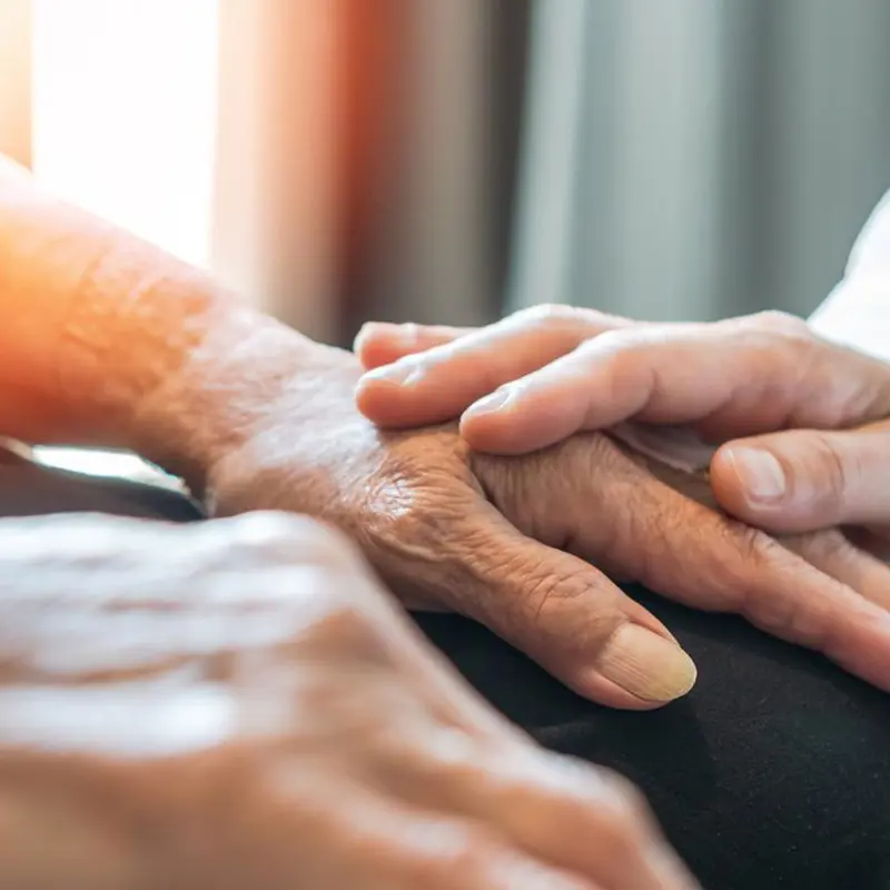 Close-up of an elderly person’s hand being comforted by a caregiver’s touch.