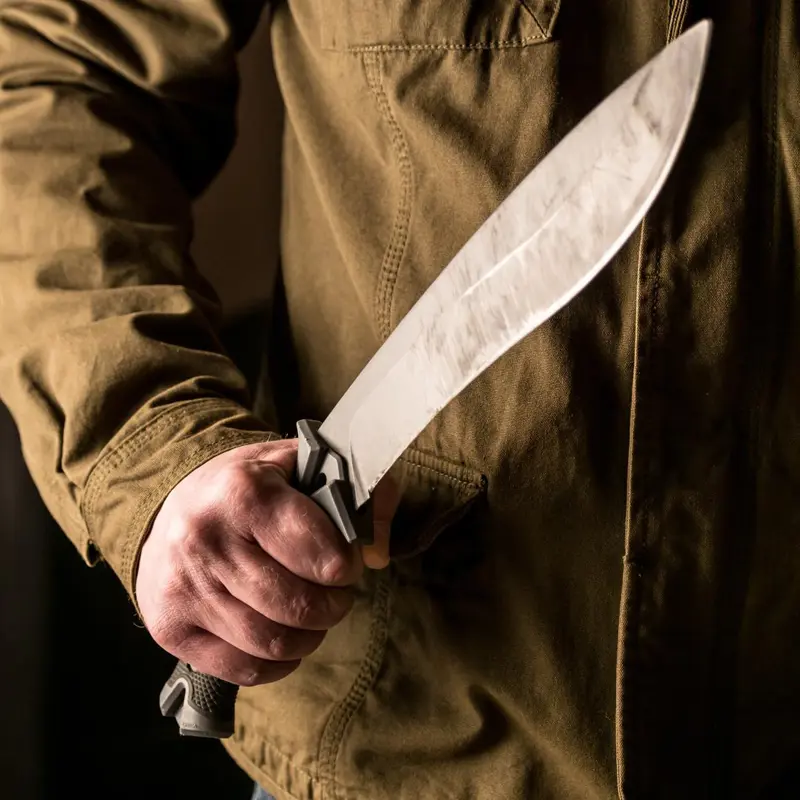 Close-up of a person holding a large knife with a firm grip.