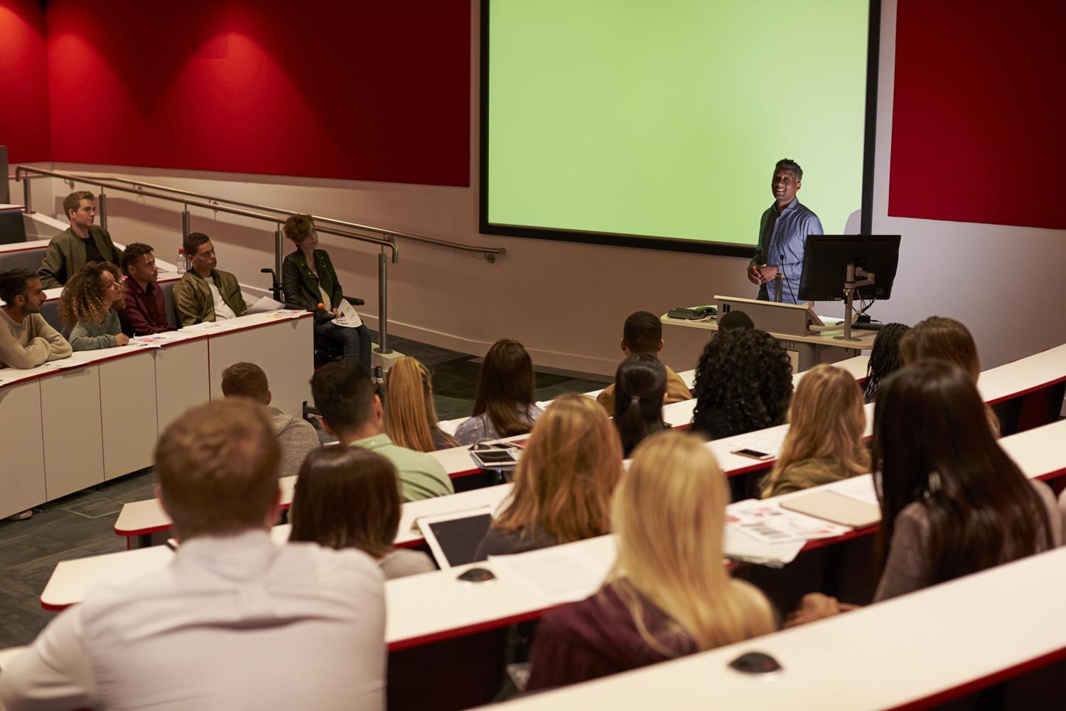 University lecturer giving a presentation to students in a large lecture hall.